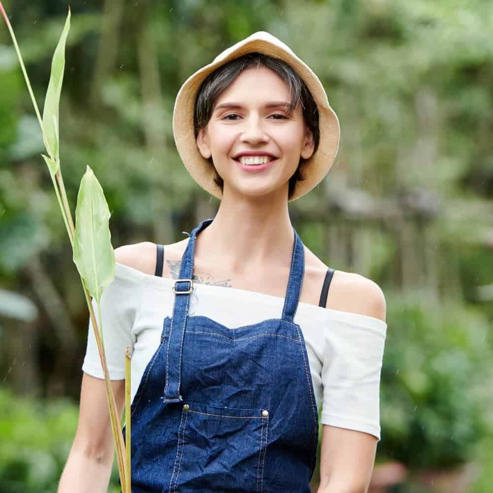 Vibrant woman smiling outdoors holding a plant, showcasing garden and landscaping work.